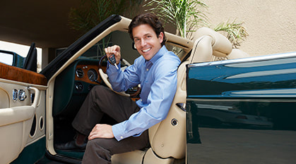 Man showing while holding a key sitting in front of convertible car photo
